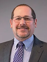David_Becker_Headshot Image of a man wearing suite and glasses